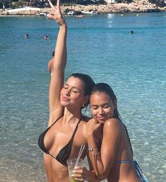 two beautiful women standing next to each other at the beach with drinks in their hands