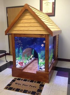 a small wooden house sitting on top of a tiled floor next to a window with fish in it