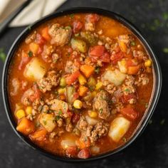 a black bowl filled with meat and vegetable soup on top of a table next to a spoon