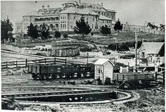 an old black and white photo of train tracks in front of a large building on top of a hill