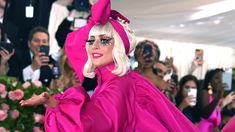 lady in bright pink outfit posing for the camera with her hands up and people taking pictures behind her