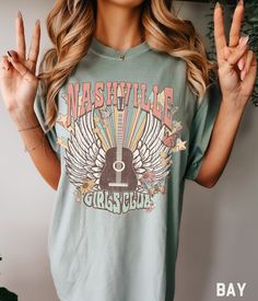 a woman wearing a green nashville t - shirt holding up two fingers