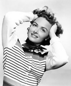 a black and white photo of a woman with her hands on her head wearing a striped shirt