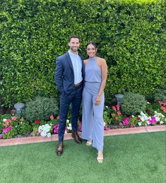 two people standing next to each other in front of a hedge