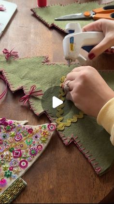 a woman is making christmas trees out of fabric and buttons on a table with other crafting supplies