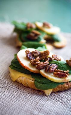 two sandwiches with cheese, lettuce and nuts on them sitting on a table