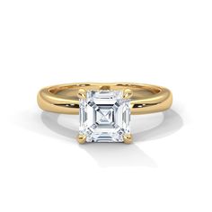 a yellow gold ring with an emerald cut diamond in the center, on a white background