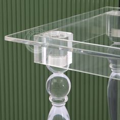 a clear glass table with a candle holder on it's base and a green striped wall behind it