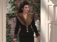 a woman in a black dress and leopard print jacket walking into a room with brick walls