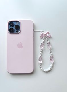 an apple phone with a pink case and beaded necklace next to it on a white surface