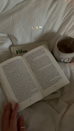 someone is reading a book in bed with their hand on top of the open book