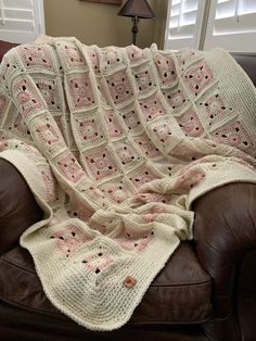 a crocheted blanket sitting on top of a brown leather couch next to a window