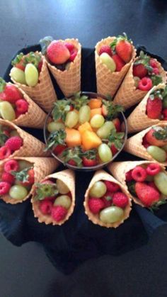 an arrangement of fruit in cones on top of a black table with a bowl of strawberries and grapes