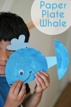 a boy holding up a paper plate whale with the words paper plate whale on it