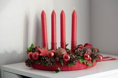 a red candle holder decorated with pine cones and christmas decorations sits on a white table