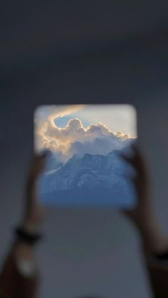 someone is taking a photo with their cell phone in front of the mountains and clouds