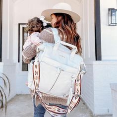 a woman carrying a baby in her back pack while walking out of a white building