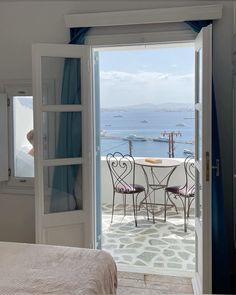 a bedroom with an open door leading to a balcony overlooking the ocean and boats in the water