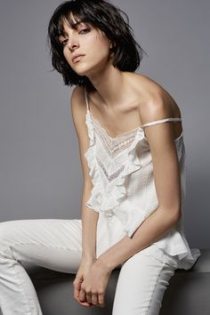 a woman sitting on top of a gray couch wearing white pants and a off the shoulder blouse