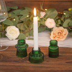 three green glass candlesticks sitting next to each other on a table with flowers