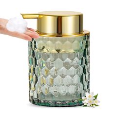 a hand is holding a glass jar with gold lid and white flowers on the side