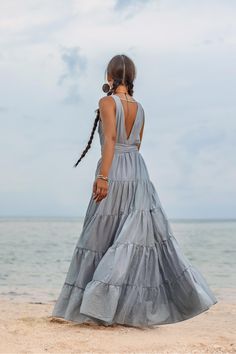 a woman standing on top of a sandy beach next to the ocean wearing a gray dress