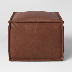 a brown leather ottoman with an attached cushion on the top and bottom, in front of a white background