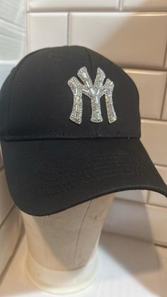 Add some sparkle to your outfit with this stunning NY Logo Rhinestone Hat. The black hat features a brilliant rhinestone accent that will catch everyone's eye. The adjustable size ensures a comfortable fit for all head sizes. Perfect for any occasion, this hat is a great addition to any wardrobe. The HaT brand ensures high quality and durability. The logo theme adds a touch of sophistication. Ideal for women who want to add a touch of glamour to their outfit. Trendy Snapback Baseball Cap With Rhinestones, Trendy Rhinestone Snapback Baseball Cap, Rhinestone Baseball Cap One Size, Adjustable Baseball Cap With Bling, Rhinestone Embellished One Size Baseball Cap, Casual Snapback Baseball Cap With Rhinestones, Trendy Rhinestone Adjustable Baseball Cap, Adjustable Rhinestone Baseball Cap With Curved Brim, Trendy Rhinestone Baseball Cap