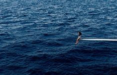 a person sitting on the edge of a boat in the middle of the ocean,