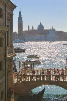 people are standing on a bridge over the water in front of some buildings and boats