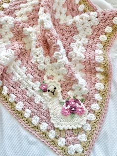 a crocheted blanket is laying on top of a white bed sheet with pink and white flowers