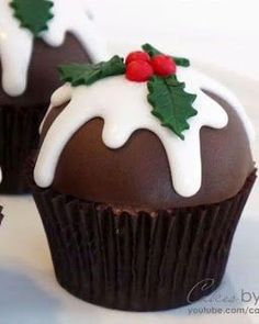 three chocolate cupcakes with white frosting and holly decorations on top, sitting on a plate