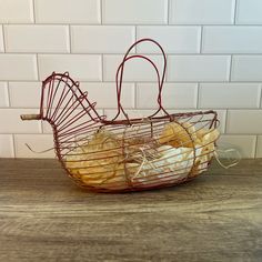 a wire basket filled with bananas sitting on top of a wooden table next to a white brick wall