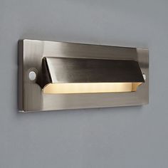 a wall mounted light on the side of a gray wall with a black and gold strip