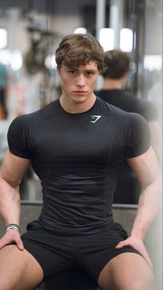 a young man sitting on top of a bench in a gym wearing a black shirt