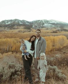 a man, woman and two children standing in a field with mountains in the background