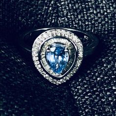 an oval shaped blue and white diamond ring on top of a black fabric background, with the center stone surrounded by smaller round diamonds