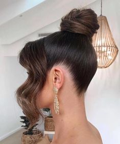 a woman with her hair in a high bun, wearing gold earrings and a black top