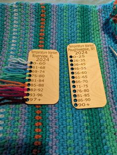 two wooden tags sitting on top of a knitted table cloth with knitting needles next to them