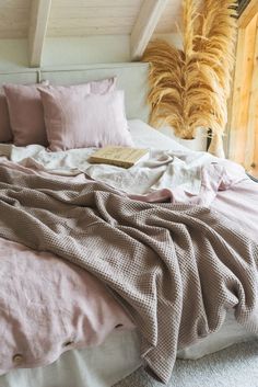 an unmade bed with pink linens and pillows in a loft space next to a window