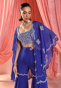 Command attention with this stunning ensemble: an embellished cape paired flawlessly with an embellished cami top and gharara bottoms. This combination of regal elegance and modern chic is perfect for making a statement at any event. Georgette Sets With Cape Sleeves For Festivals, Embellished Blue Palazzo Set For Reception, Anarkali Palazzo Set With Cape Sleeves For Festivals, Blue Palazzo Set With Sheer Dupatta For Reception, Blue Embellished Palazzo Set For Diwali, Traditional Sharara With Gota Work And Cape Sleeves, Royal Blue Designer Sharara, Anarkali Palazzo Set With Mirror Work And Cape Sleeves, Anarkali Sharara With Cape Sleeves For Festivals