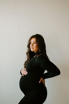 a pregnant woman poses for the camera in her black dress and high heeled boots