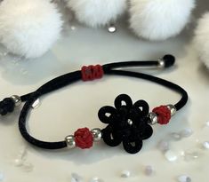 a black and red flower bracelet with silver beads on a white table next to pom - poms