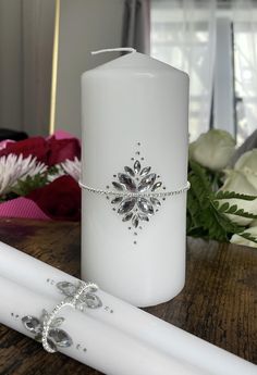 a white candle sitting on top of a wooden table next to a flower vase and pen