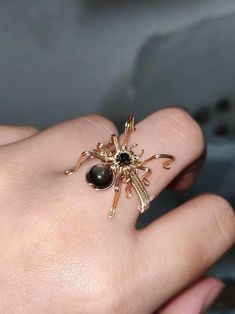 Embrace the captivating allure of the Wire Wrapped Spider Ring & Brooch, a stunning piece that brings together intricate craftsmanship and a bold statement design. This piece can be worn as a ring or a brooch, showcasing a meticulously wire-wrapped spider made from gold-plated copper wire. The spider's body is adorned with a 3mm black sandstone and a 6mm gold obsidian, creating a mesmerizing contrast of texture and depth. Each piece is fully customizable in size, ensuring a perfect fit for your Gothic Wire Ring, Goth With Gold Jewelry, Black Metal Rings For Halloween, Unique Halloween Party Jewelry, Black Brooch Jewelry For Wedding, Gothic Brooch Jewelry For Parties, Gothic Party Brooch Jewelry, Unique Black Rings For Halloween, Unique Black Halloween Rings