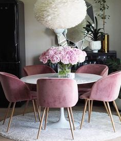 a dining room table with pink chairs and flowers in the vase on top of it