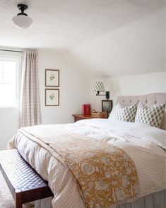 a bed sitting under a window next to a wooden bench in a room with white walls