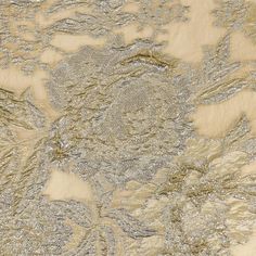 an embroidered fabric with gold and silver flowers on it, as well as the background