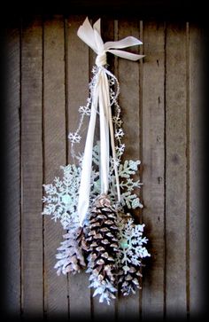 a pine cone and white ribbon hanging on a wooden wall with snowflakes attached to it