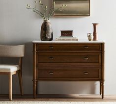 a wooden dresser with two vases on top of it next to a white chair